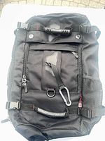 Front view of KAKA black backpack showing pockets, handles, mesh side pocket, carabiner
