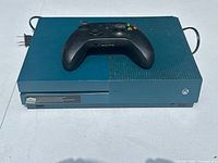 Front view of teal blue Xbox One S console with controller on top