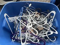 Blue bin filled with mixed plastic and metal adult hangers, showing quantity and variety