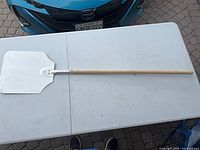 Full view of pizza peel on table showing handle length and blade shape