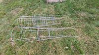 Eight large galvanized steel tomato cages lying on grass, showing full length and structure