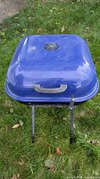Closed blue Aussie charcoal grill on foldable stand on grass