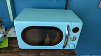 Front view of turquoise Galanz Retro microwave showing oval window and chrome handle
