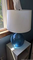 Full view of lamp showing blue glass base and white drum shade