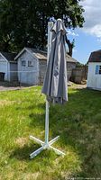 Closed grey patio umbrella on white cross base in yard