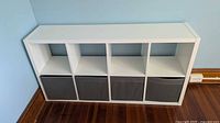 Front view of white 4x2 Kallax shelf unit with three of four grey fabric bins inserted
