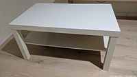 Front angled view of white IKEA Lack coffee table showing top surface, legs, and lower shelf