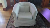 Front view of beige Ikea Tullsta armchair showing seat and lumbar cushions, slipcover skirt touching floor