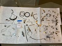 Entire assortment of jewelry spread on paper showing necklaces, bangles, rings, cuff links, earrings, bracelets and charms