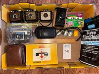 Overhead view of entire lot including five cameras, boxed Instamatic 104 outfit, flash bulbs, film, lead pouch