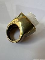 Side view of gold-tone ring showing broad sculptural band and protruding rough rock crystal