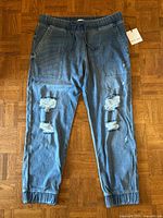 Front view of denim joggers showing ripped knees, drawstring waistband, tag attached