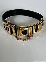 Full view of bracelet coiled showing gold plated links, heart centre, black crocodile strap, buckle, safety chain with red cabochon