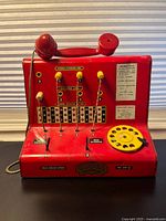 Front view of red Codeg tin switchboard phone showing rotary dial, levers, printed graphics and handset cradle