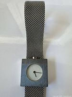Front view of watch showing square case, dial and mesh bracelet