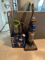 Bissell spot cleaner atop retail box next to Hoover upright vacuum