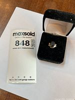 Ring in open presentation box beside lot card