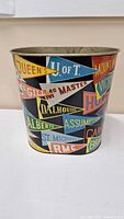 Overall view of metal wastebasket showing pennant graphics and cylindrical form