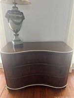Front view of walnut veneer serpentine chest showing three drawers and silver trim