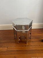 Three-quarter view of hexagonal silver metal side table on wood floor
