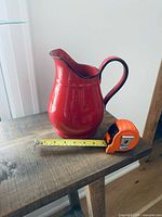Front view of red stoneware pitcher on table with tape measure showing length