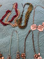 Overview of several necklaces including red resin chain, seed bead torsade and pink rhinestone bib