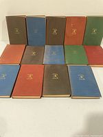 Fourteen cloth hardcovers laid flat showing gilt emblem and colour variety