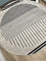 Full view of round cream rug with black stripes shown on wood floor