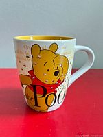 Front view of mug showing Pooh holding head, bee graphics, text, yellow interior
