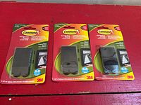 Three blister-packed Command picture hanging strip sets on red surface