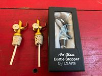 Overall lot showing two gold metal pour spouts and boxed LSArts art glass bottle stopper