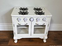 Front view of white Pottery Barn Kids farmhouse play kitchen stove with two oven doors and burners visible
