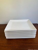 Stack of nine white square plates showing uniform design and size