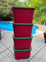 Stacked view of four red totes with green lids beside pool