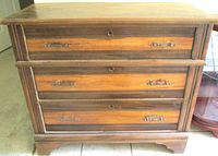 Front view showing three drawers, metal pulls, wood finish