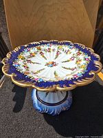 Oblique view showing full pedestal cake plate with floral, cobalt and gold design