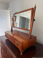 Perspective view of vanity mirror showing tilt mirror, drawers, feet, wood finish