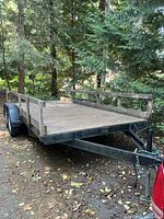 Full side view of the trailer showing wood deck, steel frame, side rails and single axle with fenders
