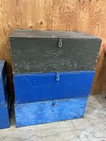 Stacked view of three painted wooden footlockers showing colors, hardware and surface wear