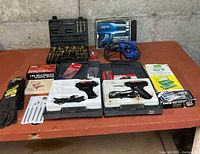 Overview of lot on table showing heat gun, soldering guns, drill bit set, extractor set, nibbling tool, pick set, gloves