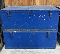 Front view of both stacked blue wood foot lockers showing latches and paint wear
