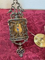 Full view of hanging lamp showing ornate metal overlay, amber glass, wiring, and ceiling canopy