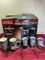 Boxed Keurig K-Elite brewer with five ceramic nautical mugs displayed
