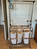 Front view of metal rolling laundry rack showing three canvas bags and top hanging rod