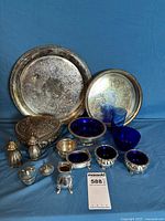 Group shot showing all blue glass pieces and silver-plated items including trays, shakers, heart box, salt cellars, condiment dish