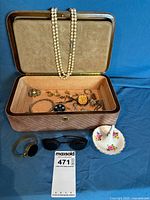 overview showing jewellery box open with contents, pearls draped, sunglasses, bracelet and saucer in front