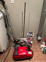 Red Miele canister vacuum with hose, wand, dustbag box and Fuller sweeper visible