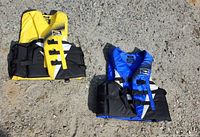 Two Fluid adult life jackets on ground, yellow and blue versions visible