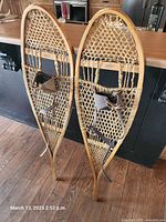 Full view of both snowshoes standing upright showing frames, webbing, bindings, brand plaque