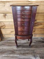 Full view of wooden jewelry armoire showing drawers, side doors and legs